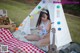 A woman sitting on a blanket in front of a teepee with a guitar.