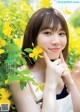 A young woman posing in front of a bush of yellow flowers.