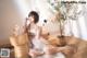 A woman in a white dress sitting on a rug next to a plant.